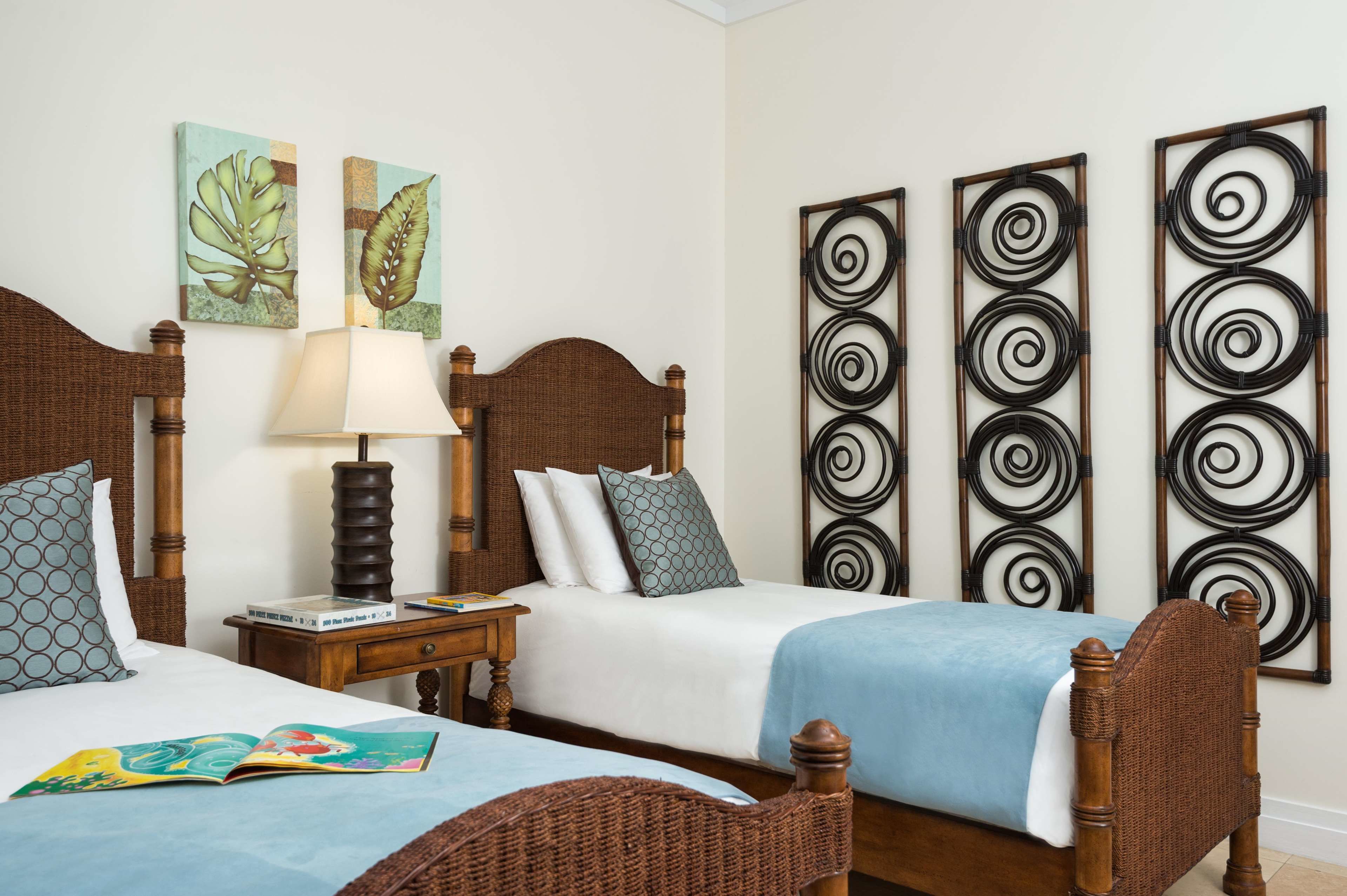 A hotel room with two wooden beds, a nightstand with a lamp, and artwork on the walls.