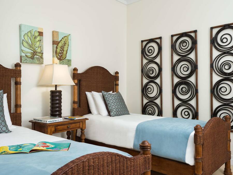 A hotel room with two wooden beds, a nightstand with a lamp, and artwork on the walls.