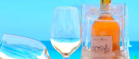 A bottle of wine, a glass, and a seashell on a table with a clear view of the ocean in the background.