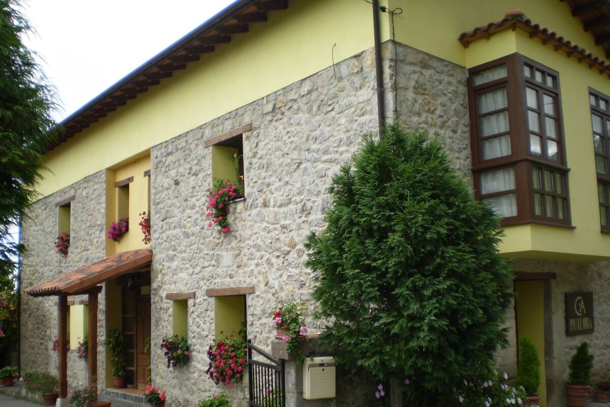A stone building with multiple windows, some with flower boxes, and a small tree in front.