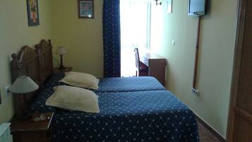 A bedroom with two beds, a desk, a chair, a television, and a window with curtains.