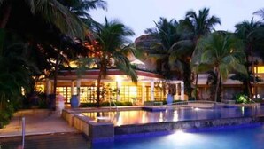 Zwembadgedeelte van een resort met palmbomen en een gebouw op de achtergrond.