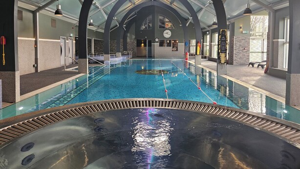 En inomhuspool med ett glastak, ett bubbelbad och en reception med en klocka och en informationsskylt.
