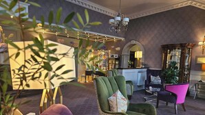 Ett väl upplyst loungeområde med olika typer av sittplatser, inklusive fåtöljer och soffor, och en receptionsdisk i bakgrunden.
