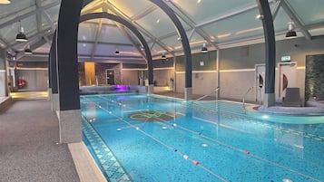 Una piscina interior con carriles delimitados, una zona de sauna y un mostrador de recepción.