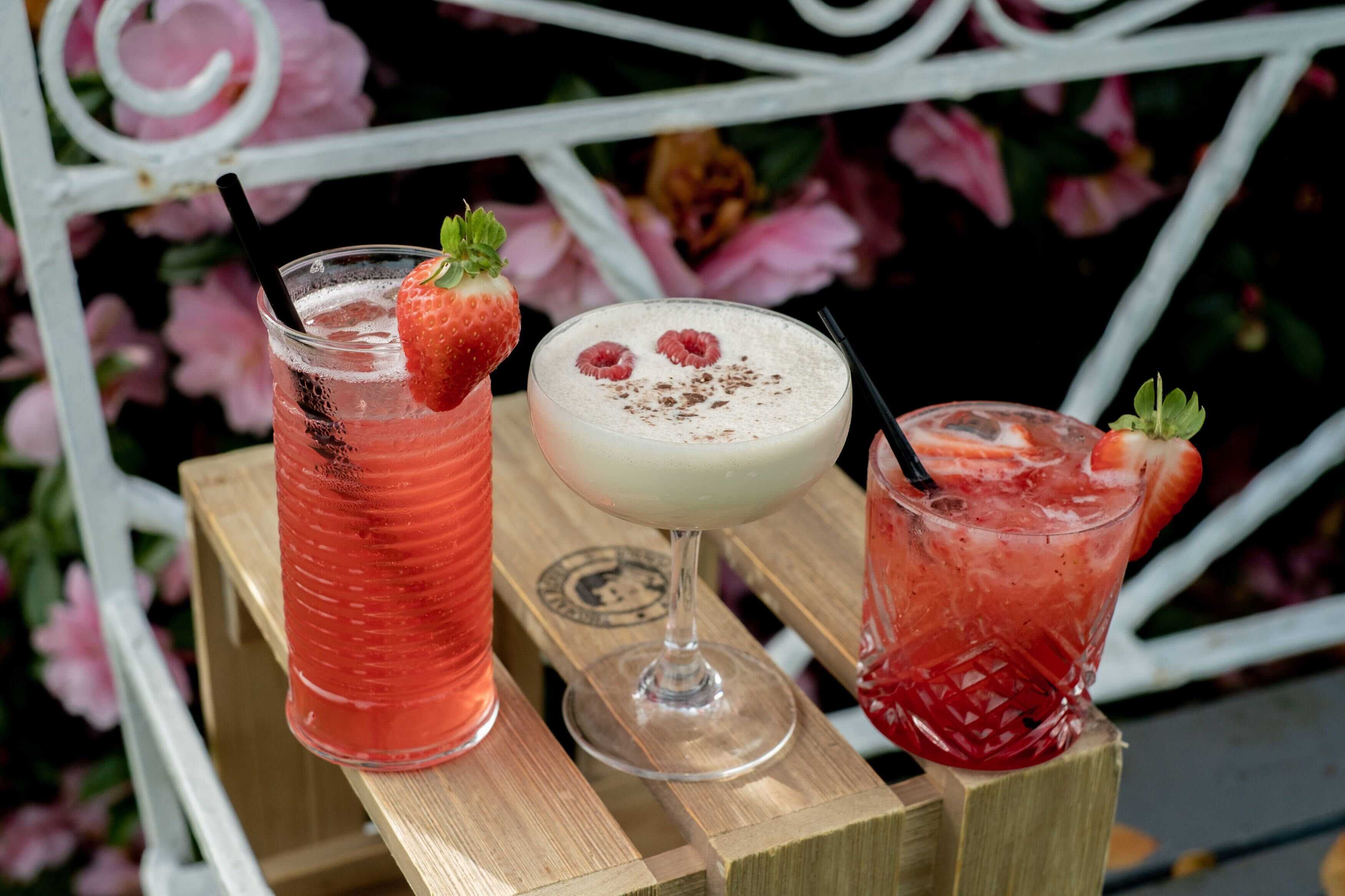 Three drinks on a wooden table with a metal railing in the background.