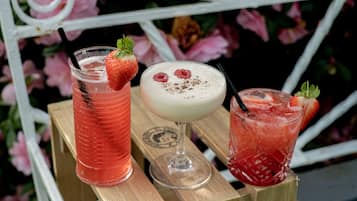 Three drinks on a wooden table with a metal railing in the background.