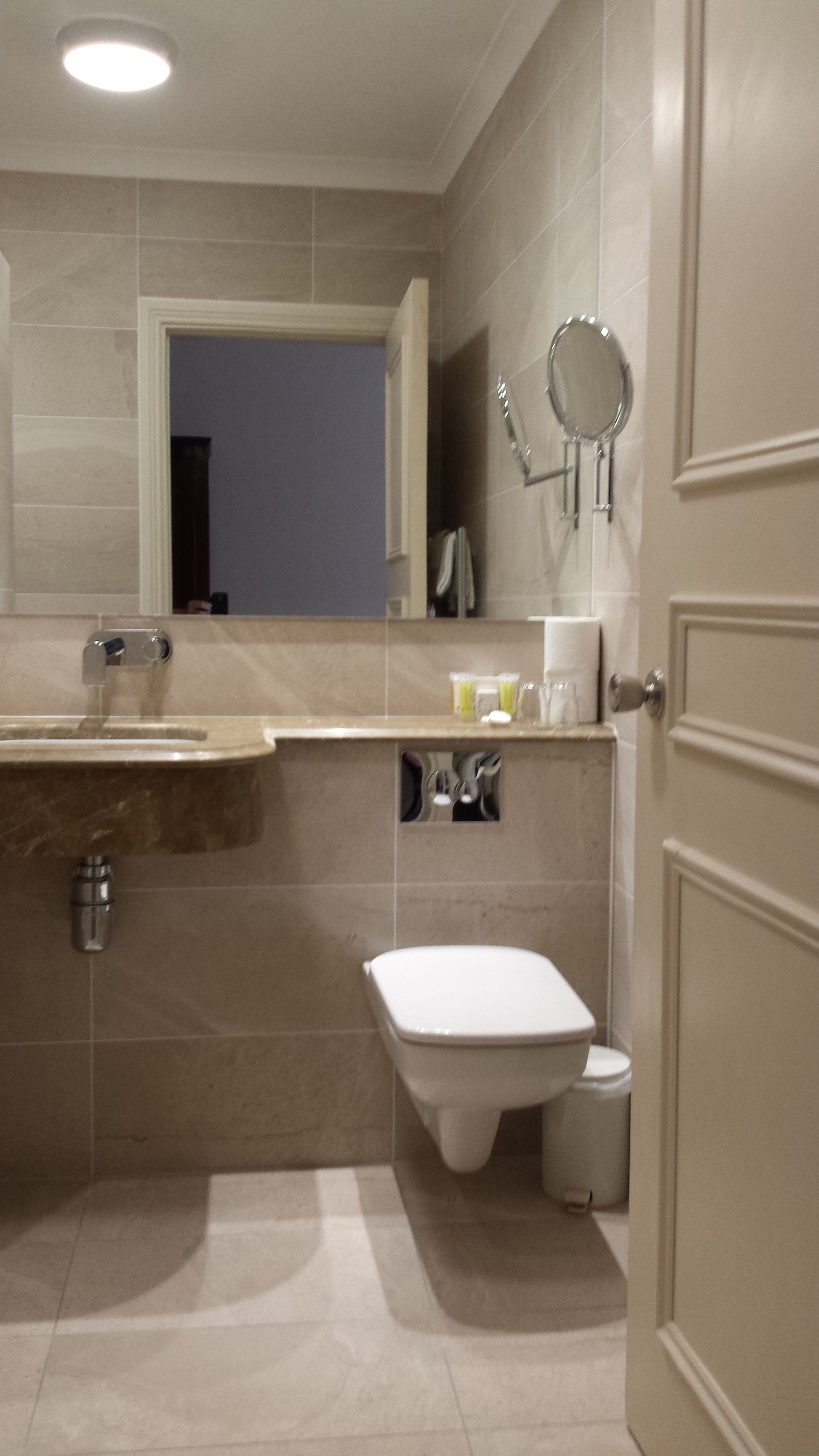 A bathroom with a sink, mirror, toilet, and a door.