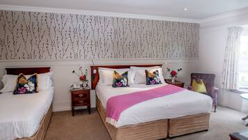 A hotel room with two beds, a large window with curtains, and a floral wallpaper design.