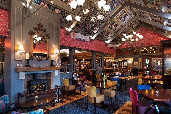 A restaurant with a brick fireplace, multiple tables and chairs, and a bar area.