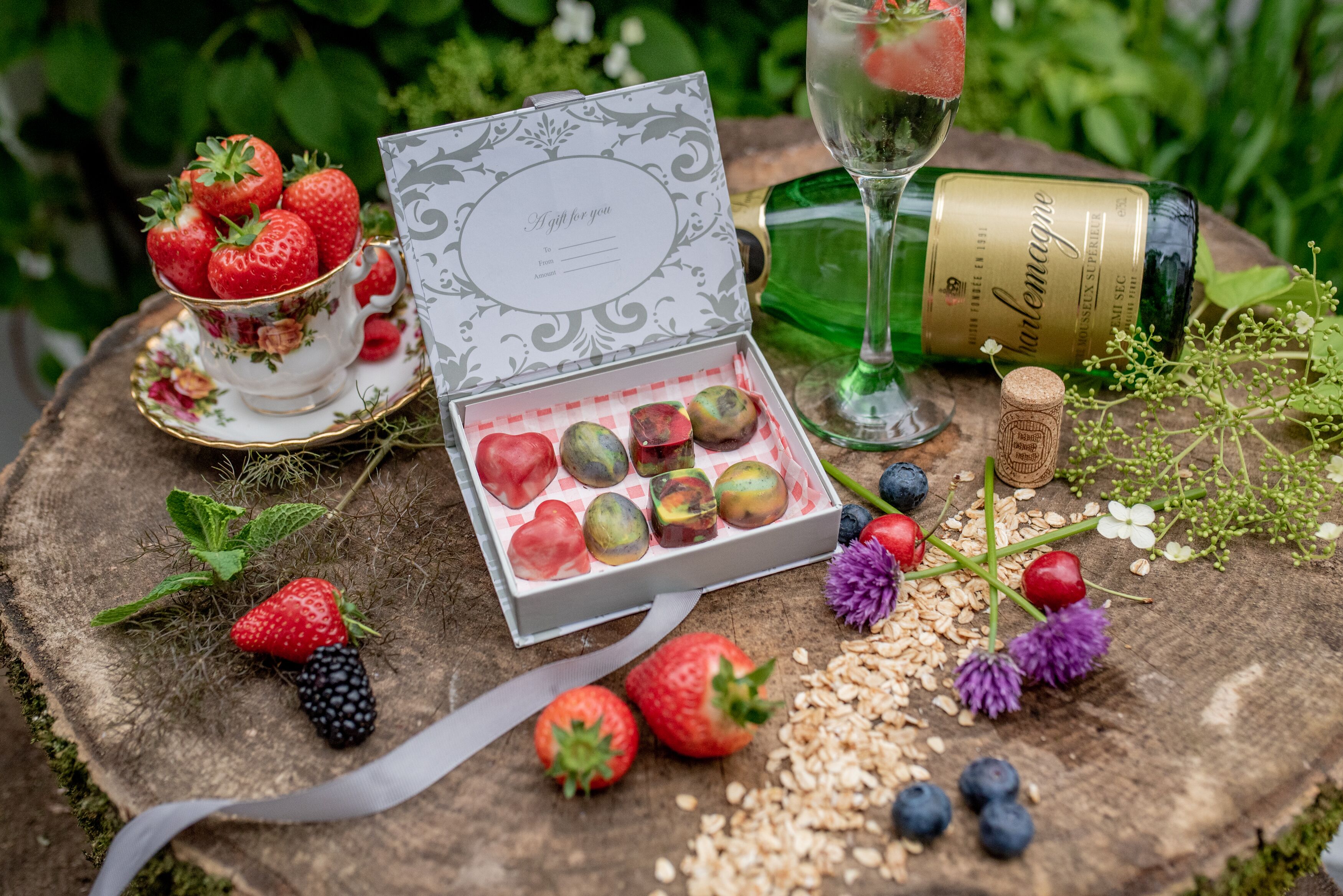 A table with a tea set, a bottle of wine, a gift box, and various fruits and berries.