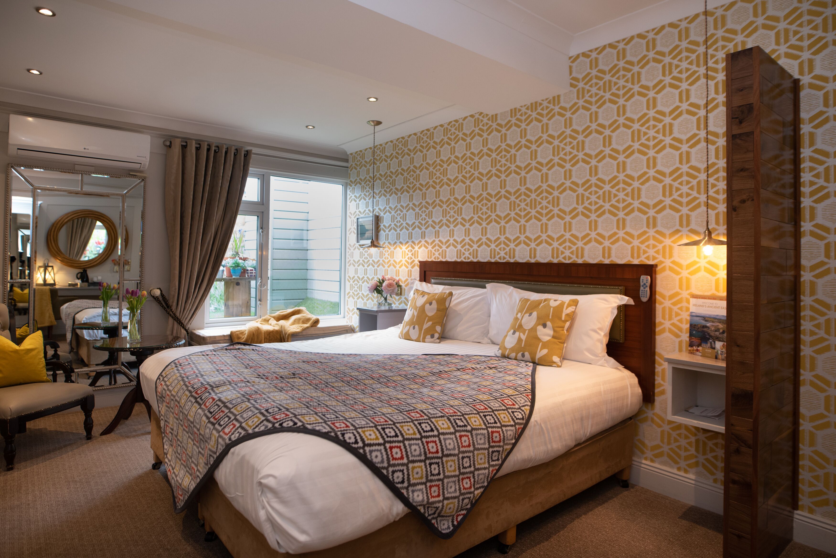 A bedroom with a large bed, bedside tables, a chair, a mirror, and a window with curtains.