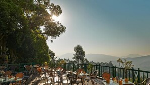 An outdoor dining area with tables and chairs, surrounded by greenery and overlooking a mountainous landscape. - Club Mahindra Munnar (Devikolam)