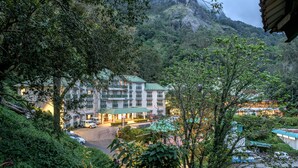A hotel with multiple floors, a parking area, and lush greenery surrounding it. - Club Mahindra Munnar (Devikolam)