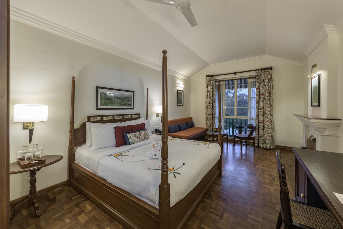 A four-poster bed with a wooden frame, a bedside table with a lamp, a sofa, a chair, and a fireplace.