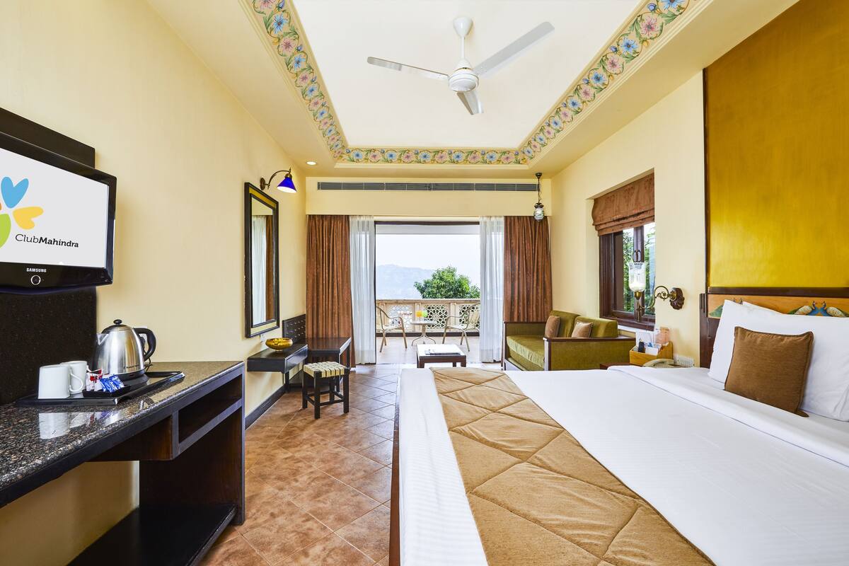 Habitación de hotel con cama, escritorio, silla y un televisor que muestra 'ClubMahindra'.