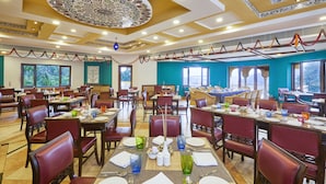 A spacious dining area with multiple tables and chairs, large windows, and a decorative ceiling. - Club Mahindra Kumbhalgarh (Rajsamand)