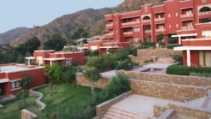 A red multi-story hotel with balconies, situated on a hillside with a landscaped garden. - Club Mahindra Kumbhalgarh (Rajsamand)