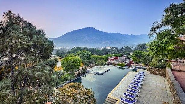 A rooftop infinity pool with a view of a mountain, surrounded by lush greenery and a clear sky. - Club Mahindra Kumbhalgarh (Rajsamand)