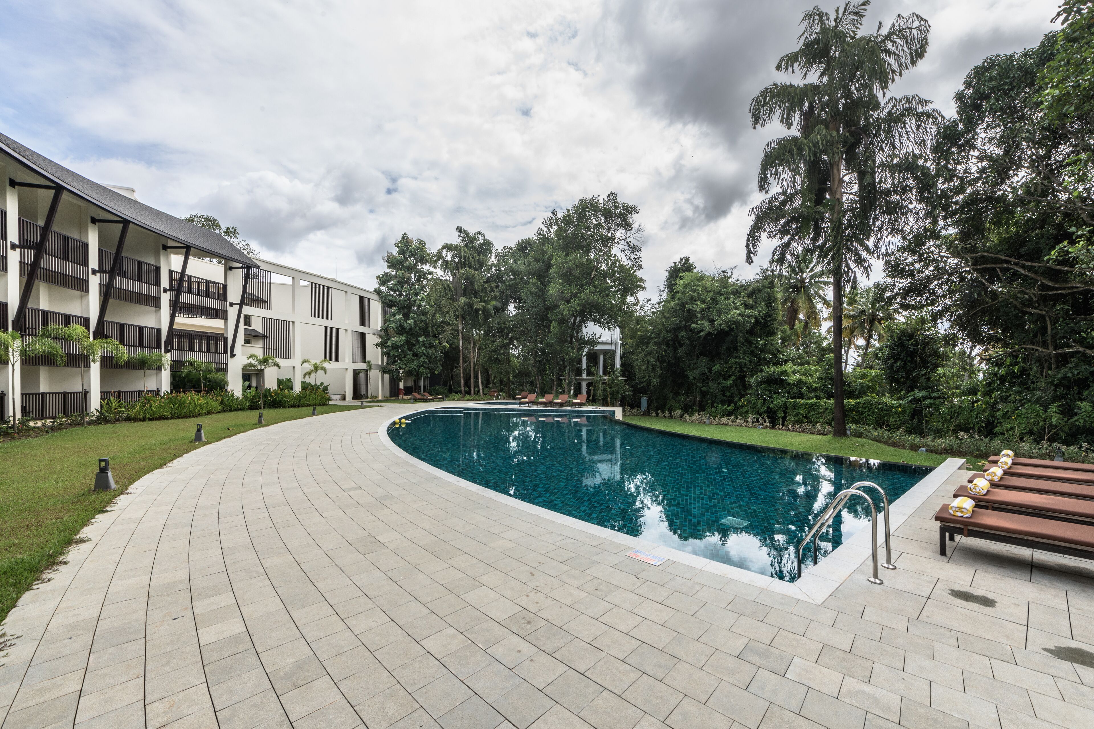 A swimming pool with a curved edge, surrounded by a paved walkway and lounge chairs.