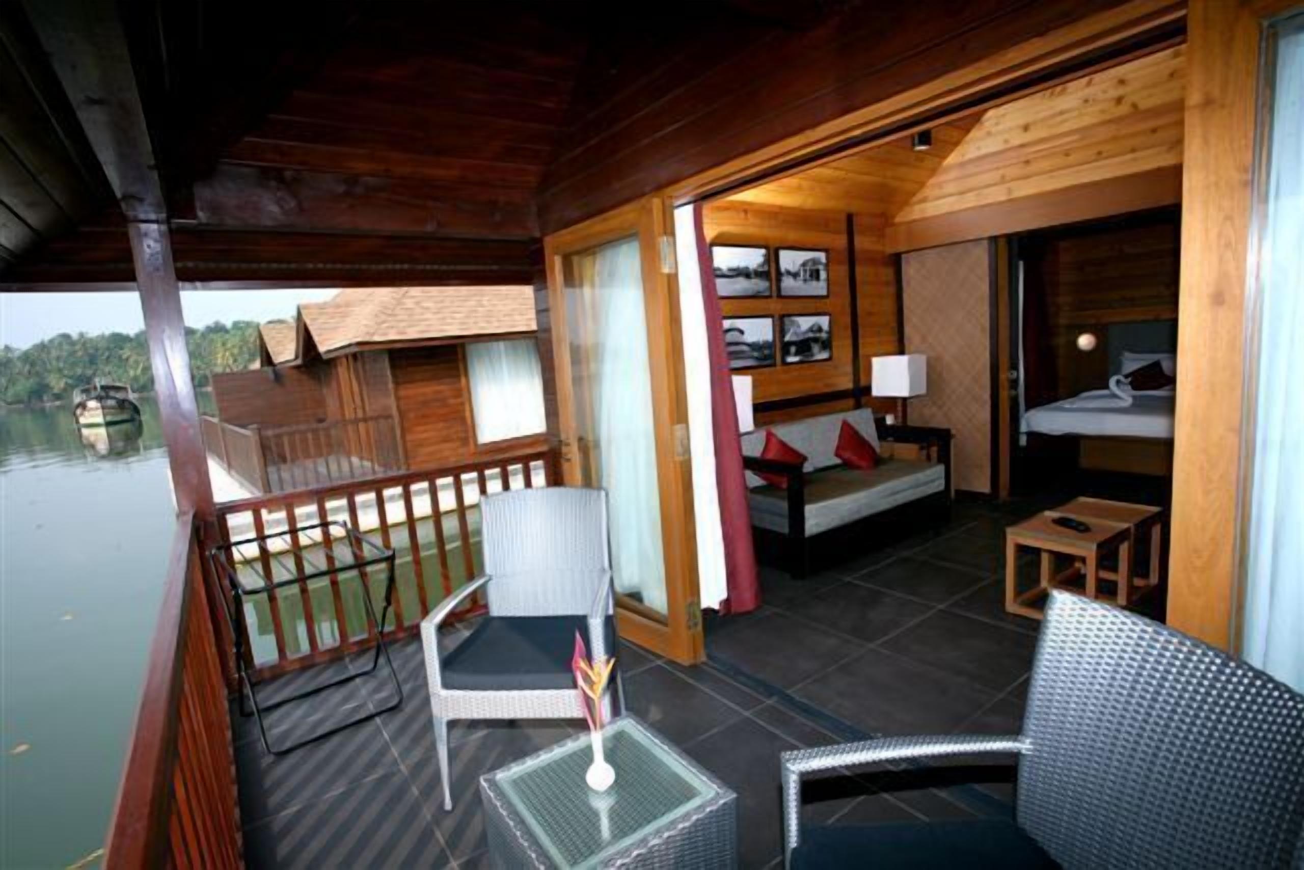A wooden cabin with a balcony, a small dining area, and a bedroom with a bed and a nightstand.