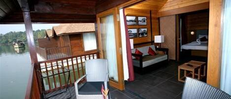 A wooden cabin with a balcony, a small dining area, and a bedroom with a bed and a nightstand.
