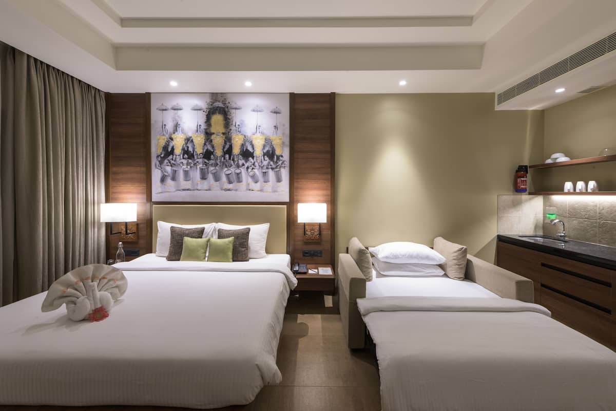 Ein Hotelzimmer mit zwei Betten, einem Gemälde an der Wand, einem Nachttisch, einer Lampe, einem Spiegel und einer Minibar.