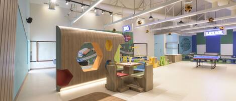 A modern indoor play area with a wooden play structure, a ping pong table, and colorful seating.