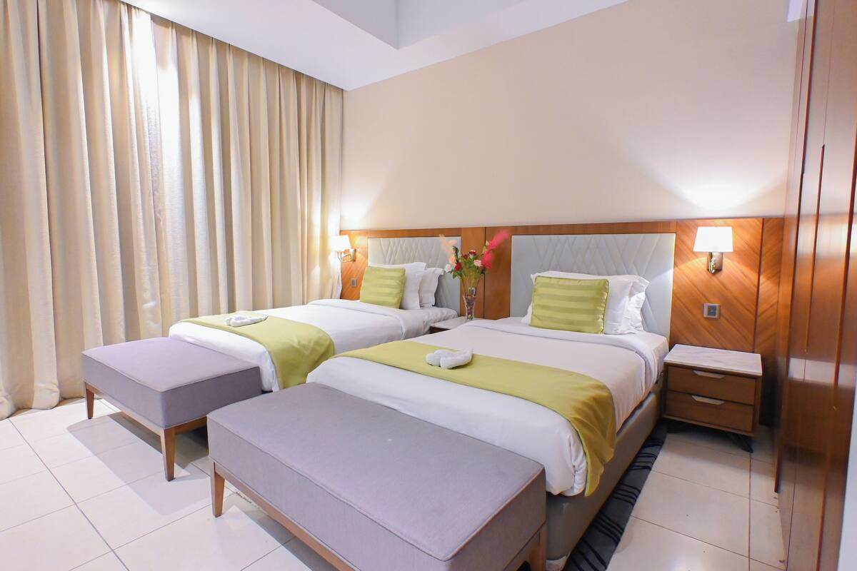 Habitación de hotel con dos camas, una mesita de noche y un ventanal con cortinas.