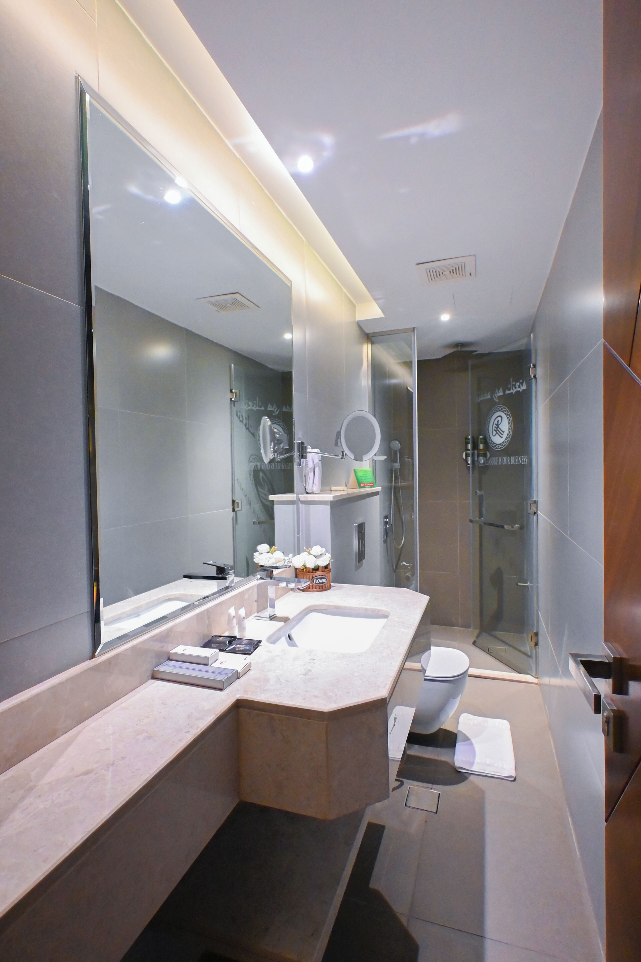 A modern bathroom with a large mirror, a glass shower enclosure, and a vanity with a sink and towel rack.