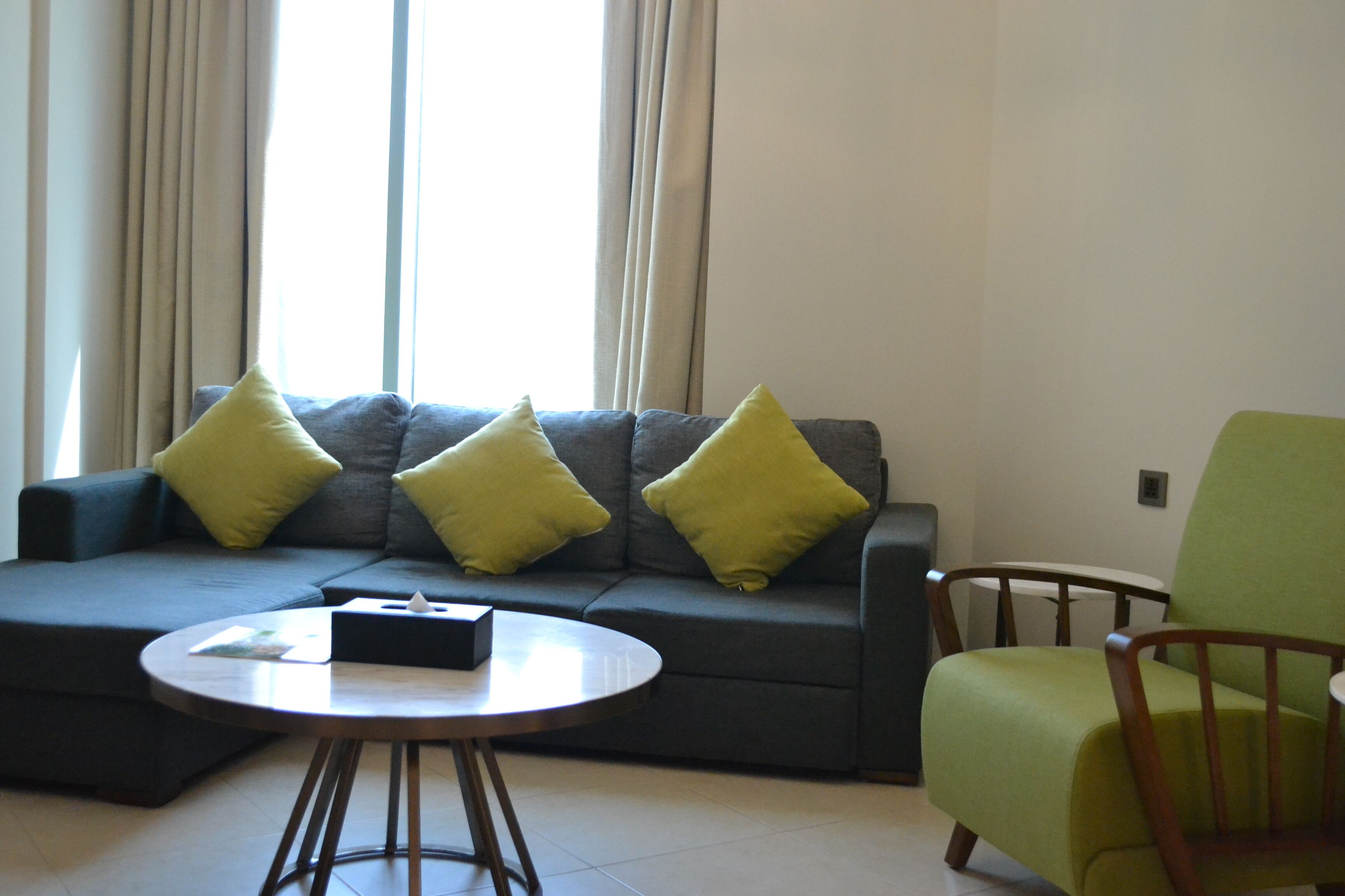 A living room with a grey sofa, green cushions, a round wooden coffee table, and a green armchair.
