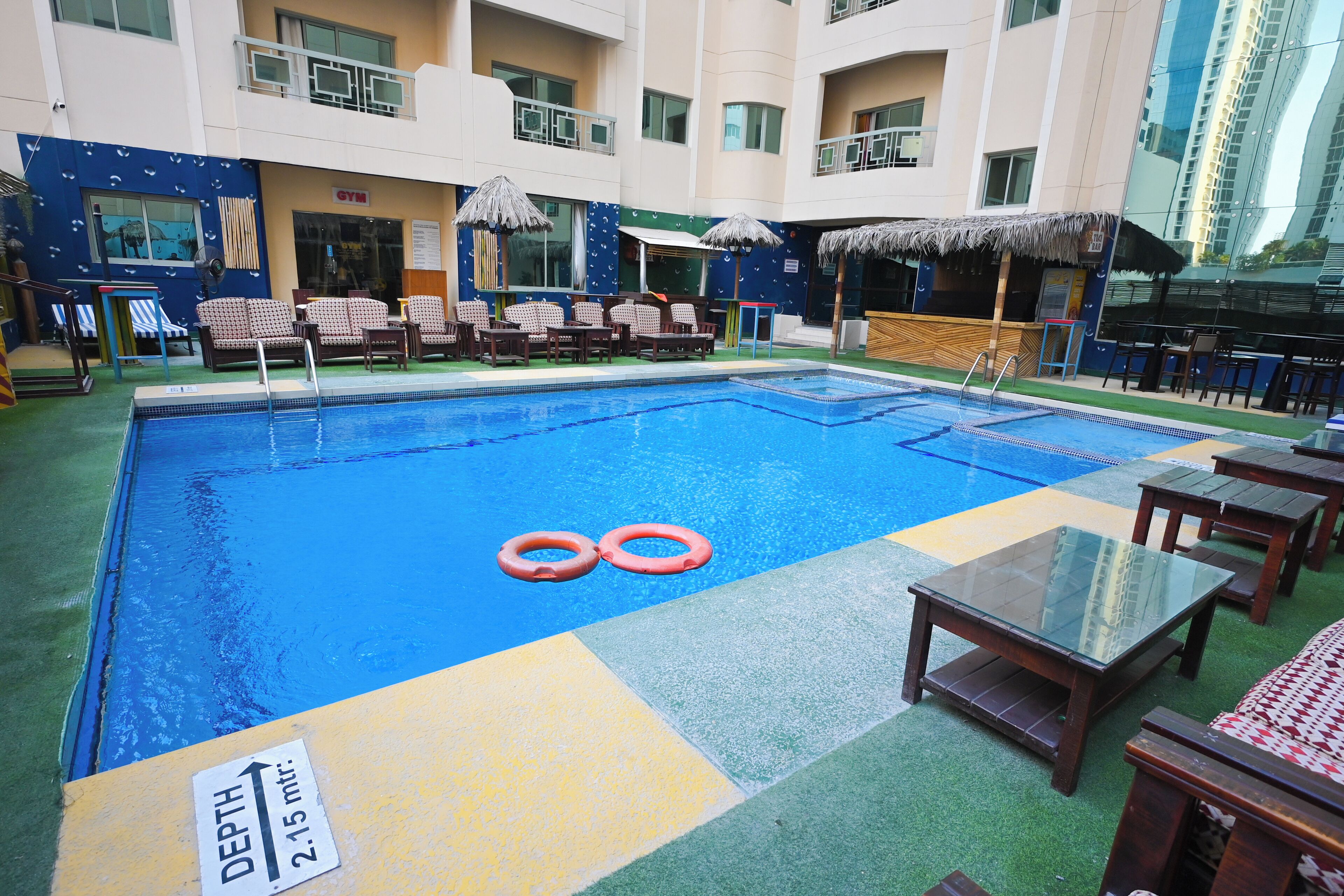 Un espace piscine équipé de chaises longues, d’un bar et d’un panneau indiquant une profondeur de 2,15 mètres.