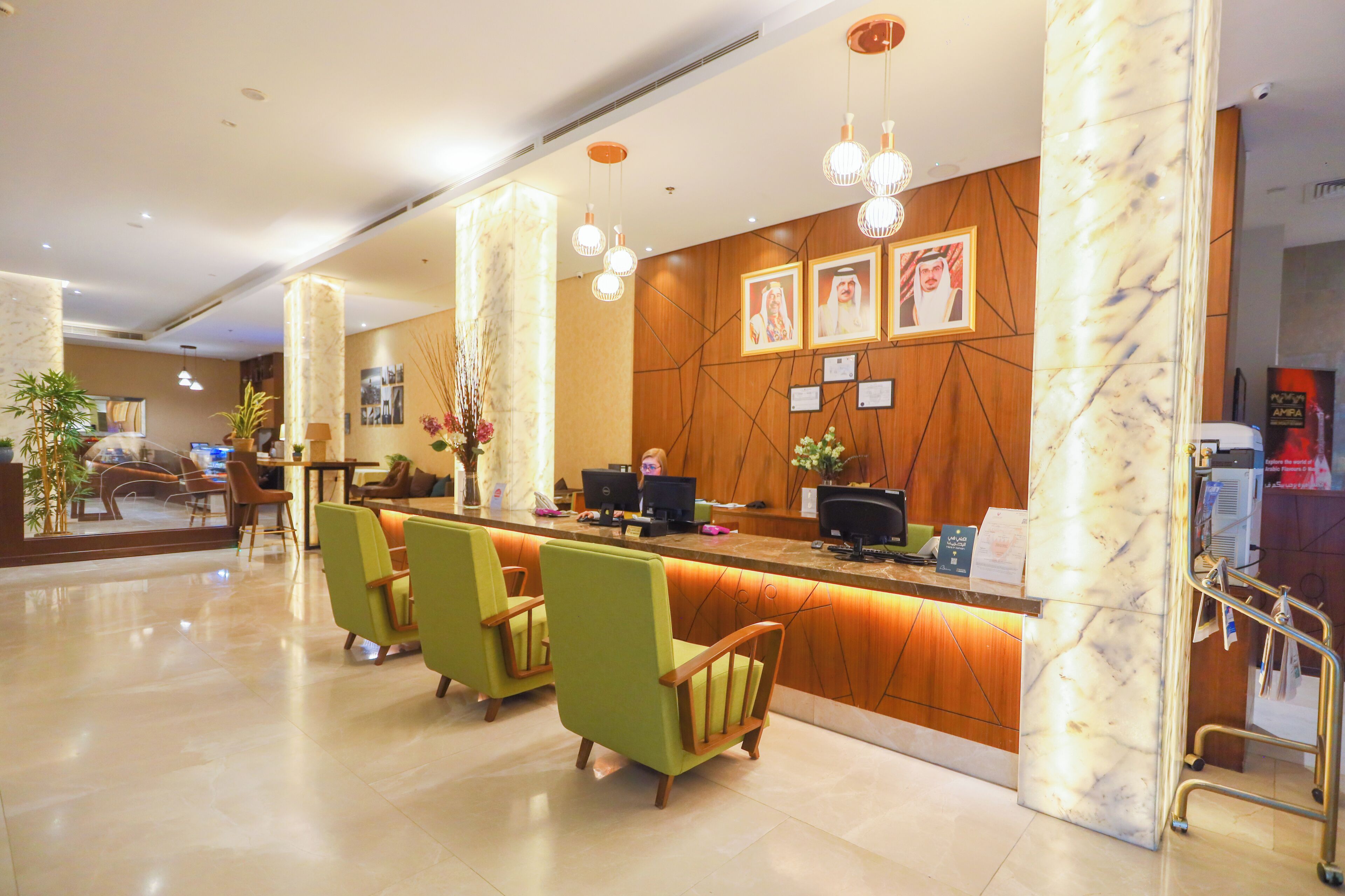 A hotel reception area with a marble reception desk, green chairs, and a wooden wall with framed pictures.