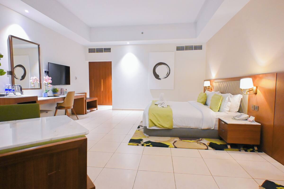 Una habitación de hotel con cama, mesita de noche, lámpara y escritorio con silla.