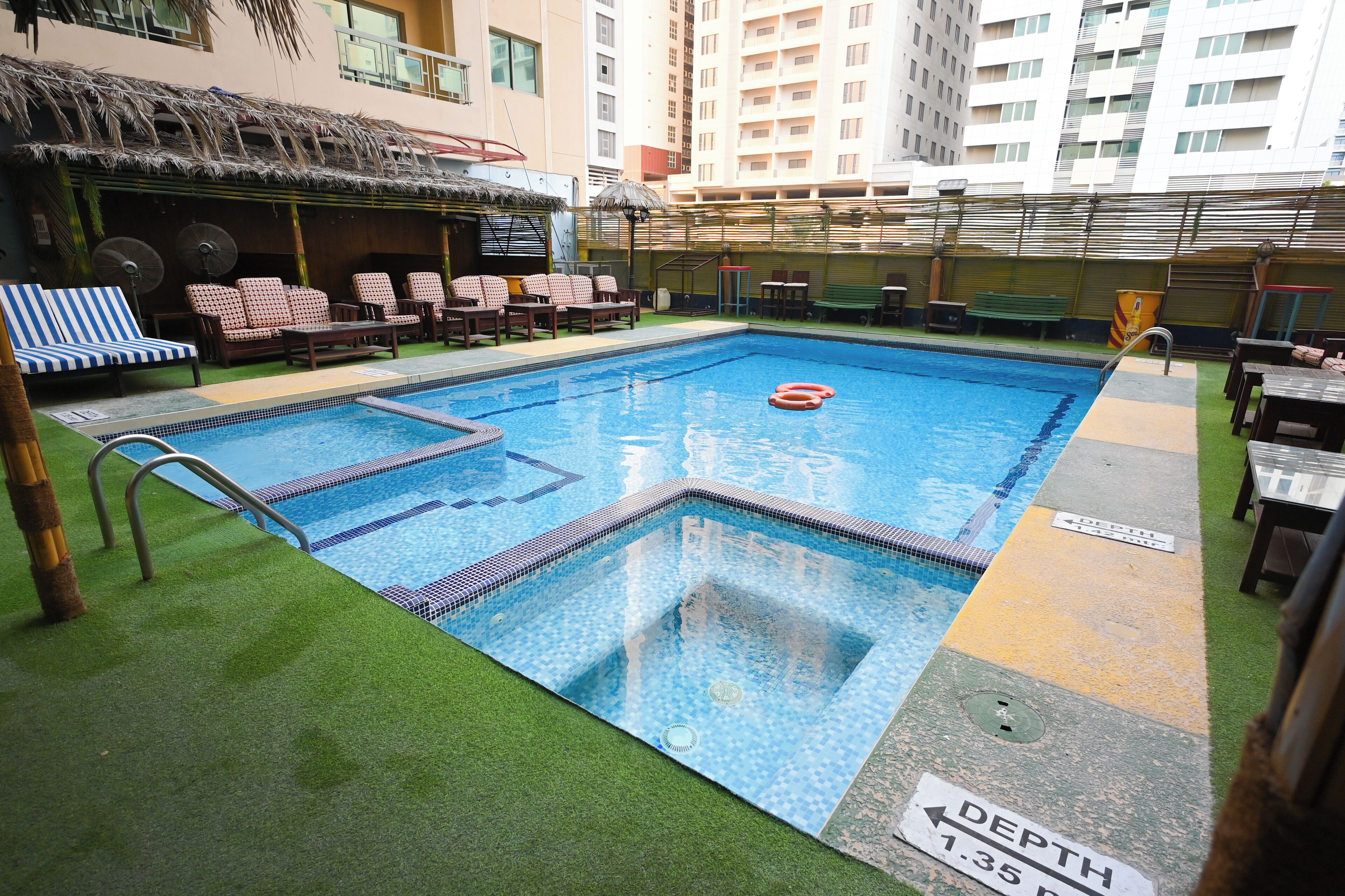 Piscina con indicador de profundidad, sillas de descanso y zona de estar con techo de paja.
