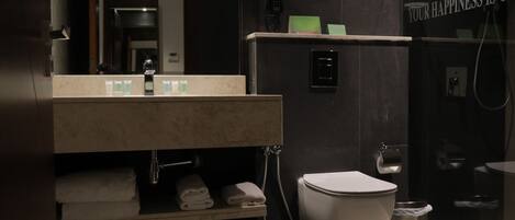 A modern bathroom with a sink, mirror, and toilet. There is a towel rack with folded towels, a shower area, and a sign on the wall.
