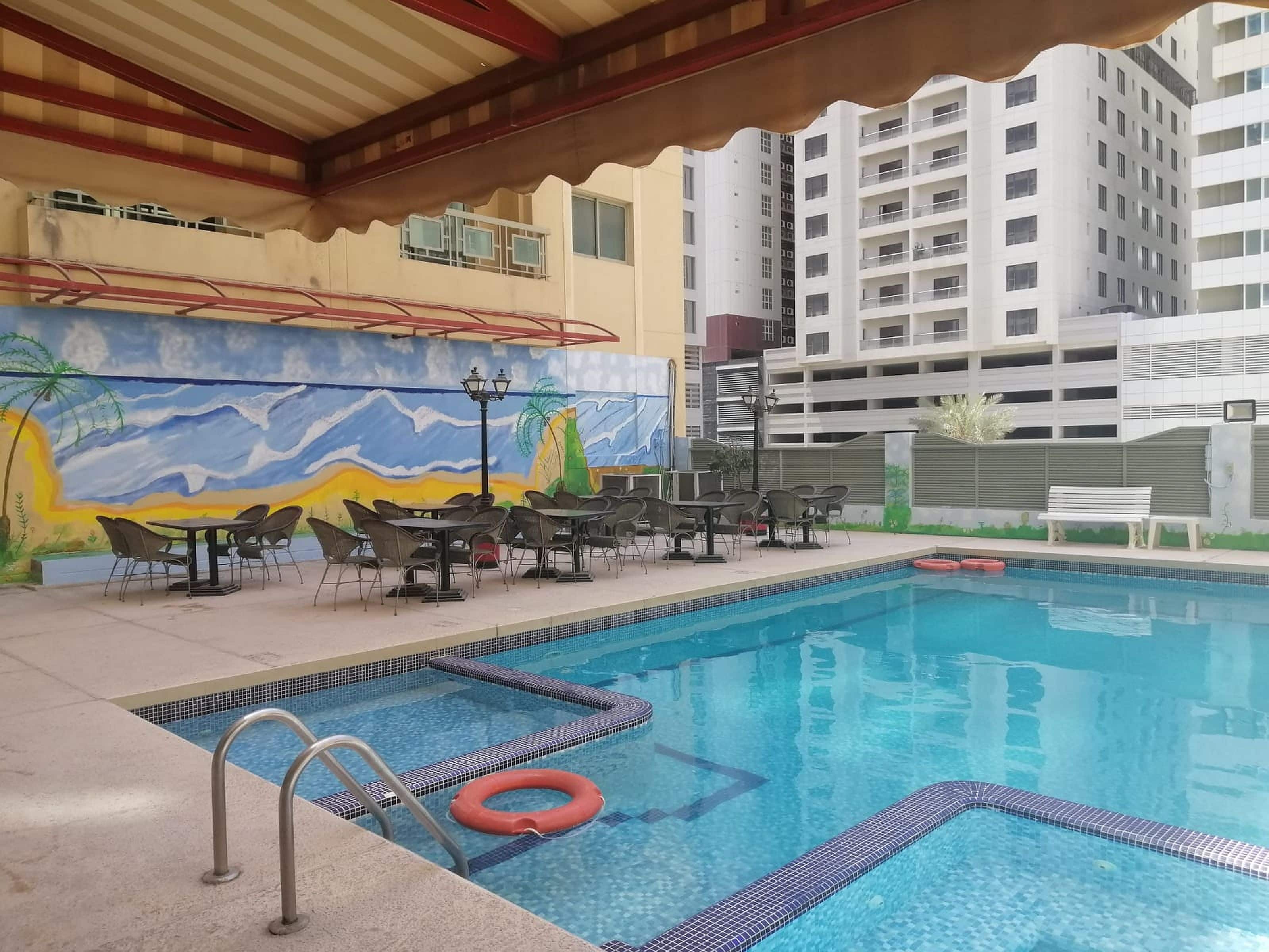 An indoor swimming pool with tiled edges, surrounded by lounge chairs and tables.