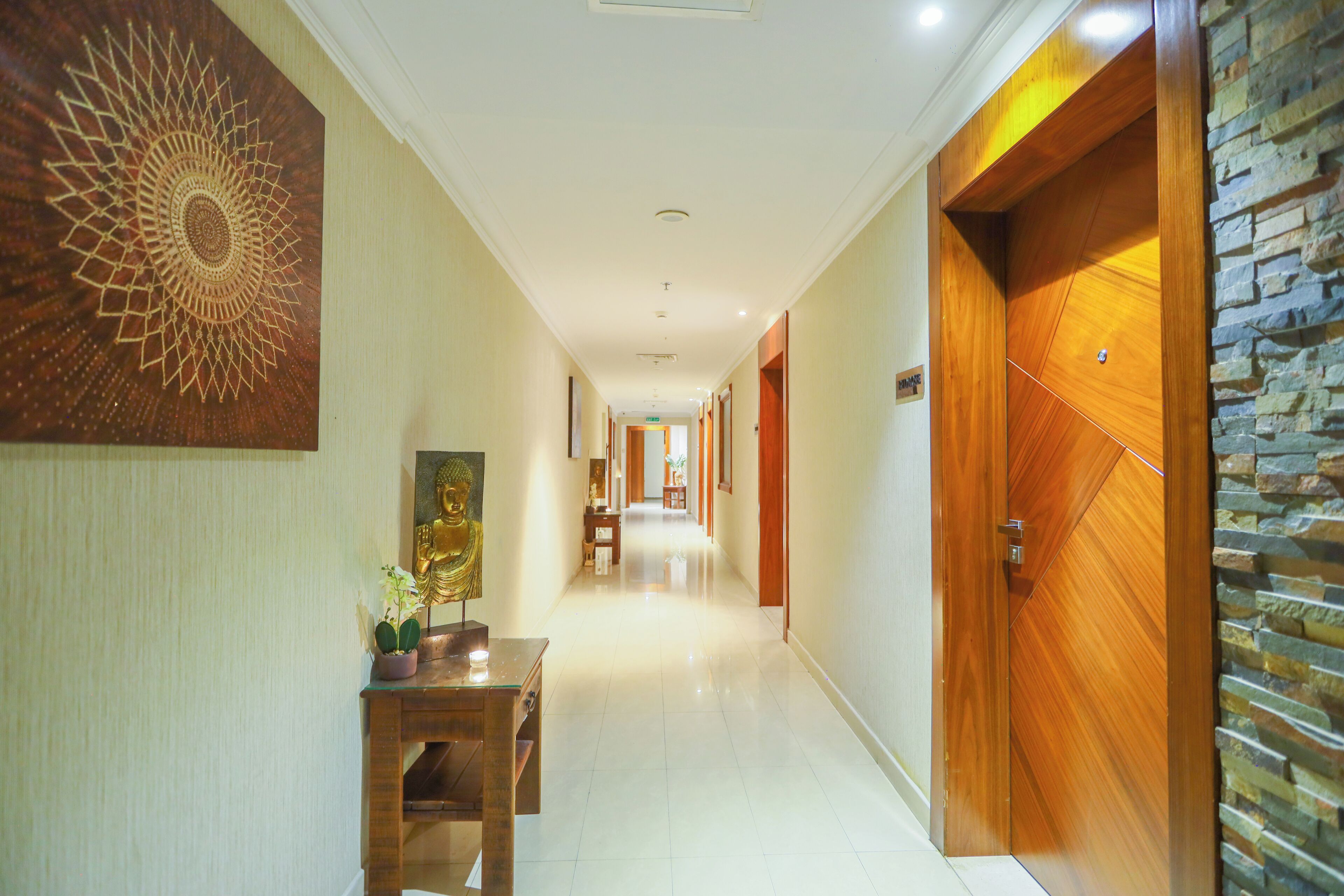 Un couloir d’hôtel avec une porte en bois, une statue de Bouddha et un élément décoratif mural.