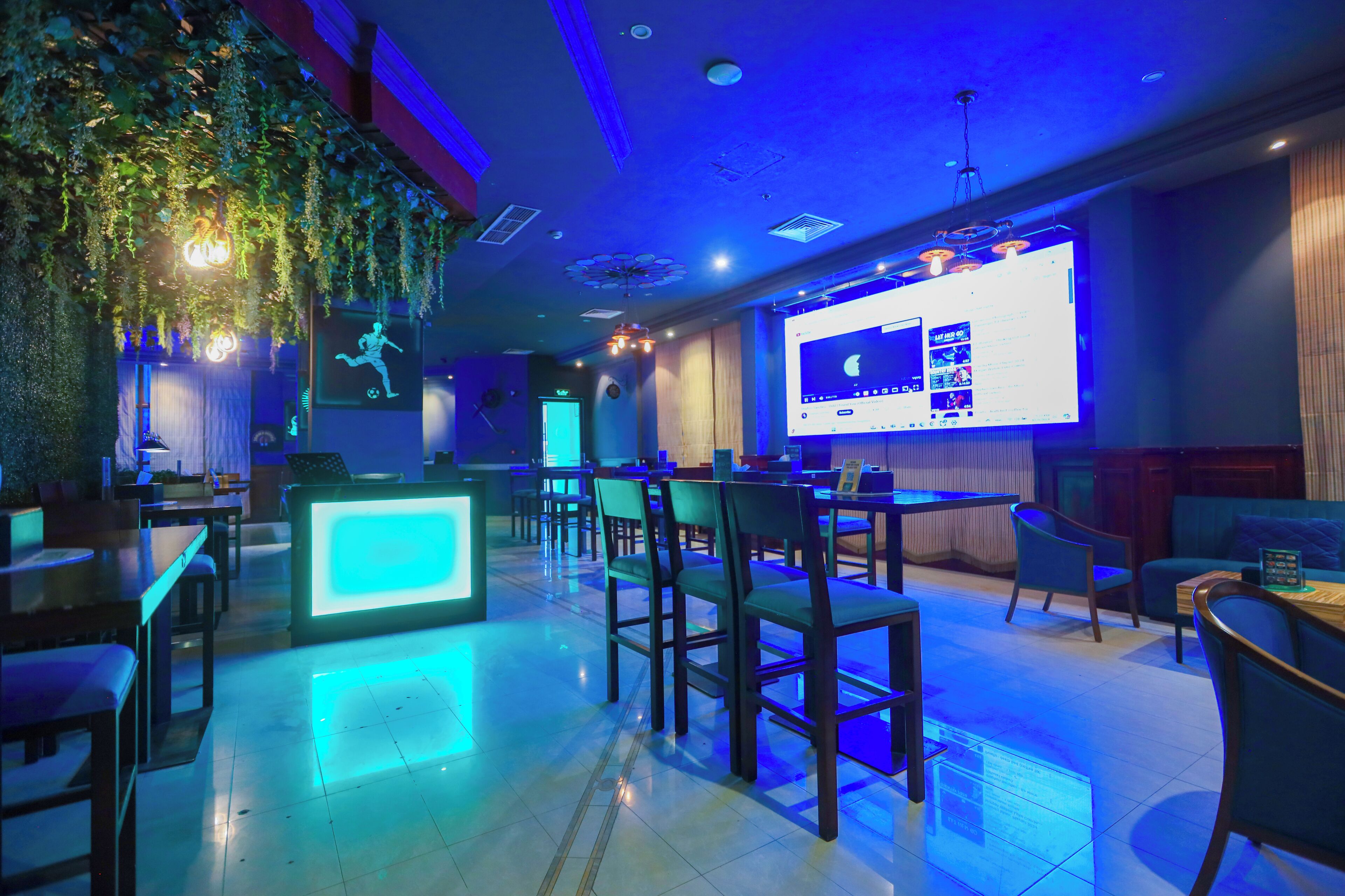 Un espacio lounge moderno con barra, asientos y una pantalla grande mostrando contenido.
