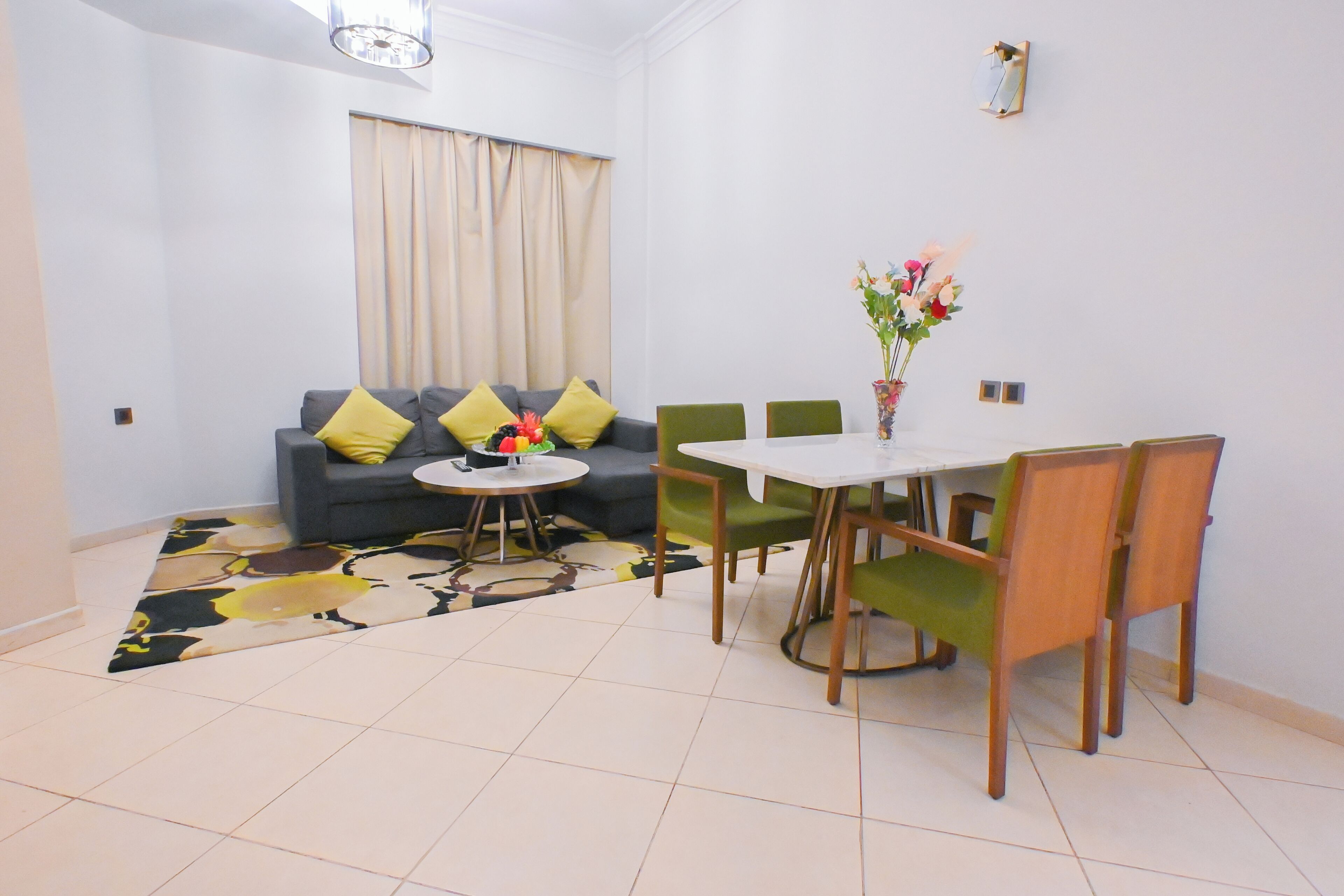 Una sala de estar con un sofá, sillas verdes, una mesa de comedor y un jarrón con flores.