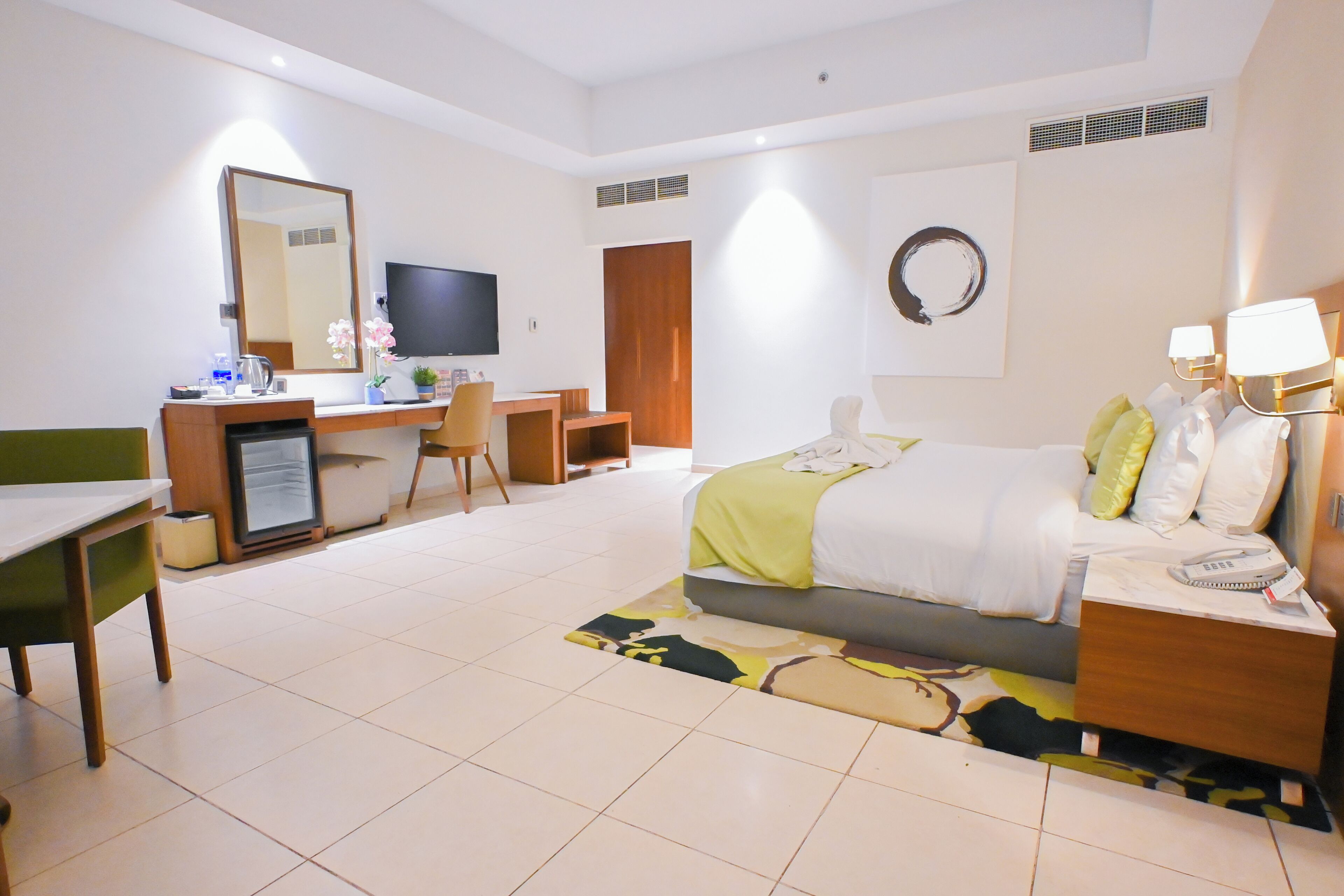 A hotel room with a bed, bedside table, desk, chair, television, and a large mirror.