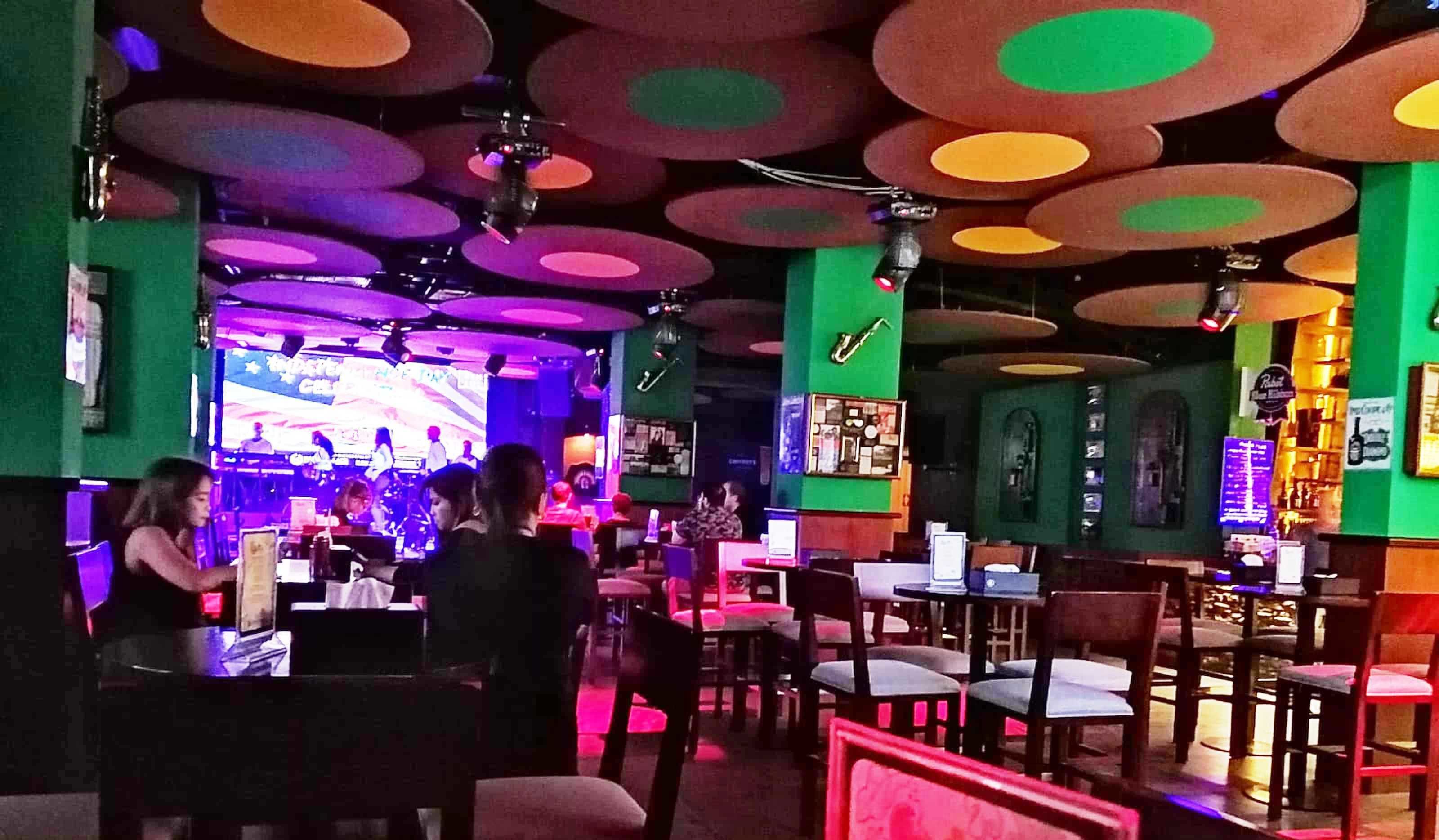 Un restaurante con un interior vibrante, que cuenta con un escenario para presentaciones en vivo y una zona de comedor informal con mesas y sillas.