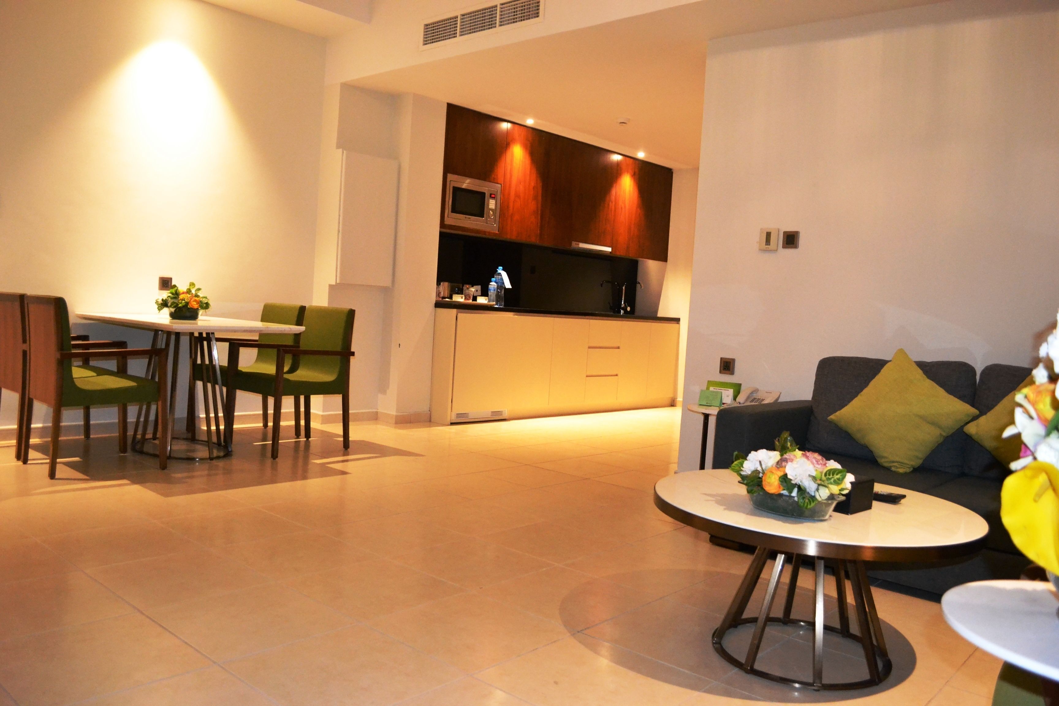 A modern living room with a dining area, a kitchen in the background, and a sofa with a flower arrangement.
