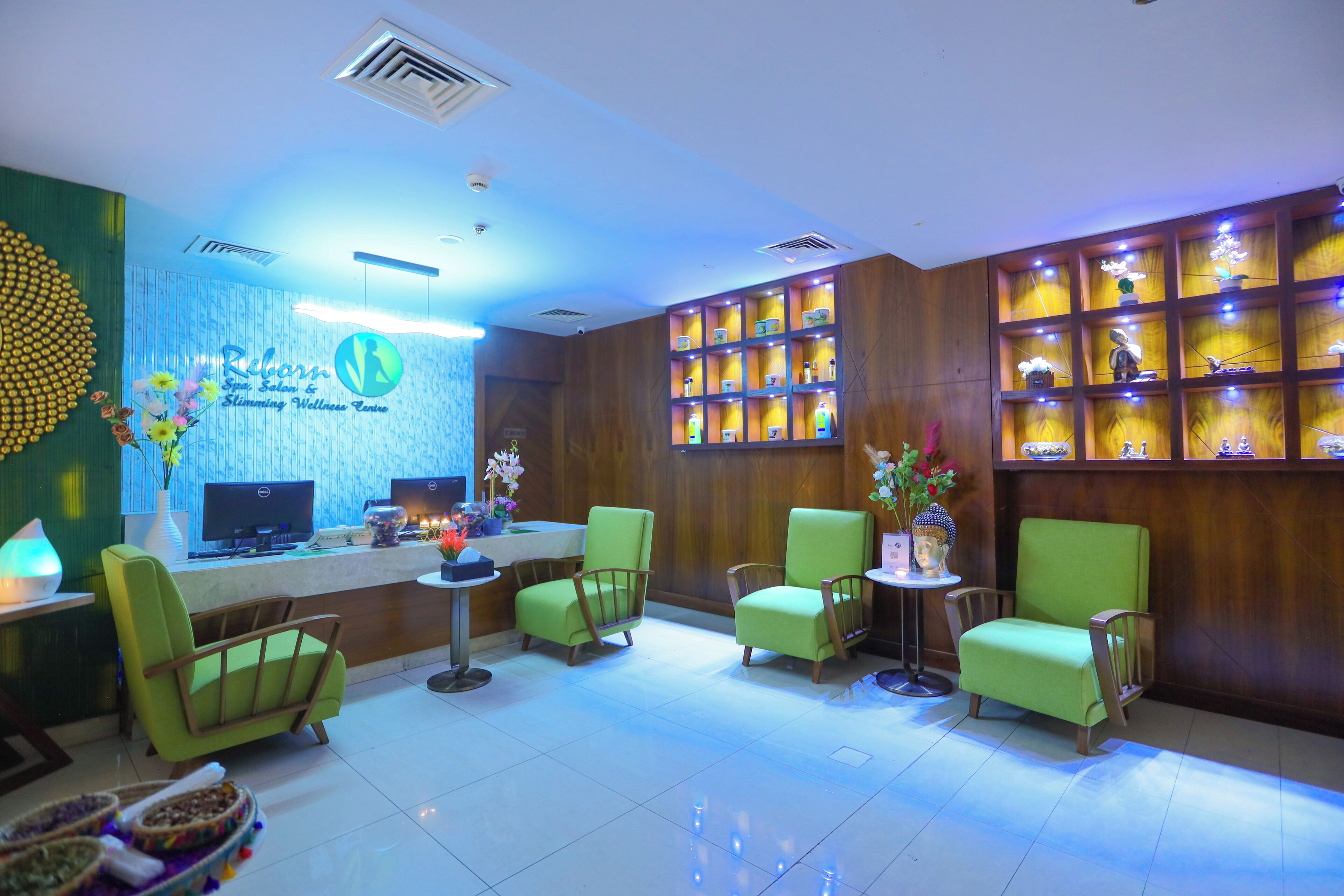A reception area with a reception desk, green chairs, a small table with a vase of flowers, and shelves with decorative items.