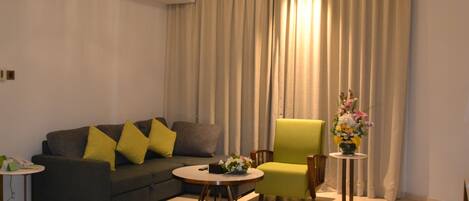 A modern living room with a grey sofa, a green armchair, a round coffee table, and a small side table with a vase of flowers.