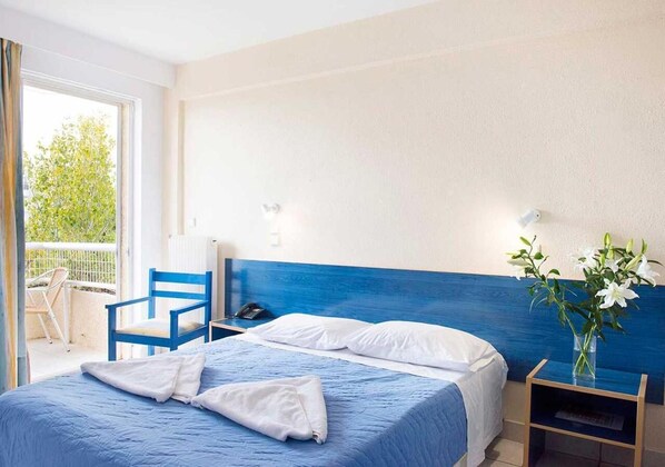 A hotel room with a bed, a chair, a bedside table, and a view of the outdoors. - Stefanakis Hotel & Apartaments (Vari-Voula-Vouliagmeni)