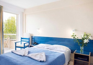 Habitación de hotel con cama, una silla, mesita de noche y vistas al exterior.