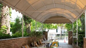 An outdoor patio with a covered seating area, tables, and chairs. - Stefanakis Hotel & Apartaments (Vari-Voula-Vouliagmeni)