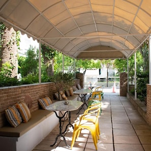 An outdoor patio with a covered seating area, tables, and chairs. - Stefanakis Hotel & Apartaments (Vari-Voula-Vouliagmeni)