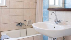 A bathroom with a bathtub, a sink, and a window. - Stefanakis Hotel & Apartaments (Vari-Voula-Vouliagmeni)